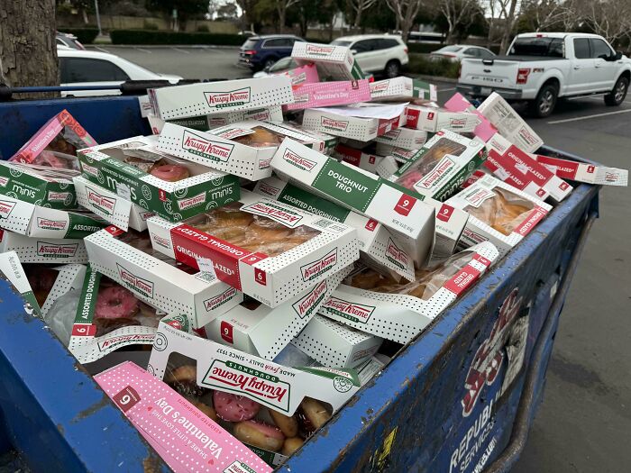 A dumpster overflowing with Krispy Kreme boxes, a mildly interesting scene in a parking lot.