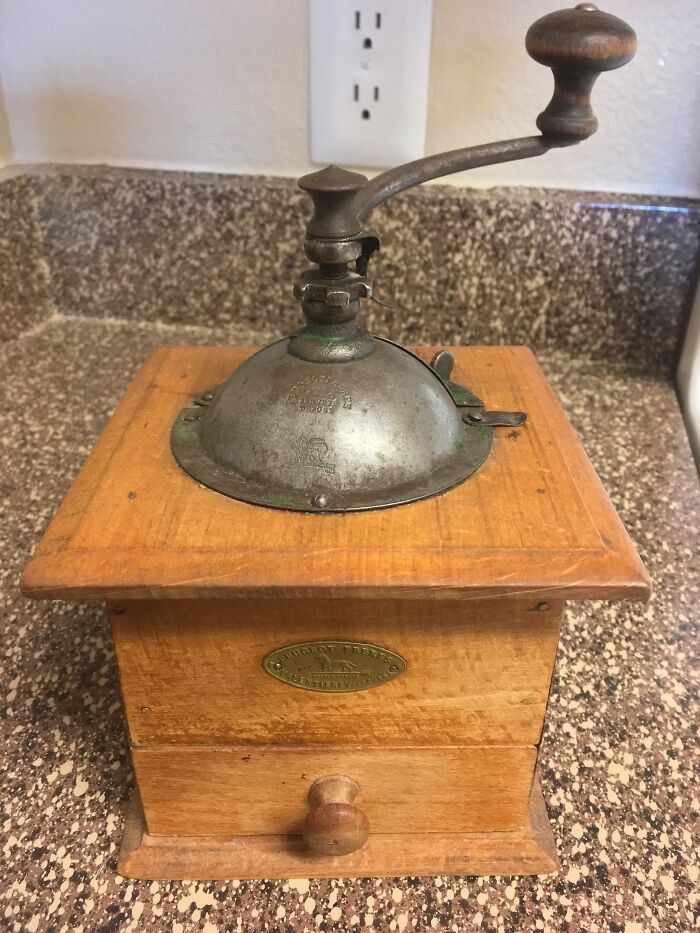 Vintage coffee grinder with a wooden base and metal handle, showcasing cool-old-things style on a speckled countertop.