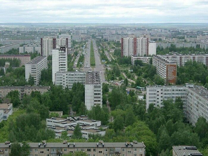 Urban landscape with dense high-rise buildings and greenery under a cloudy sky.
