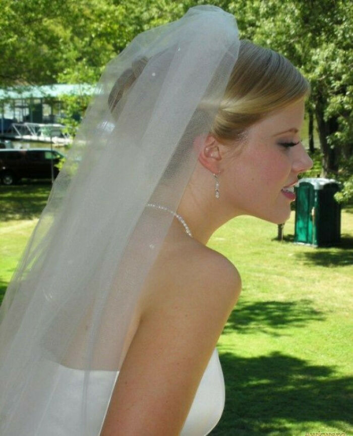 Bride in a white dress and veil posing outdoors in an awkward family photo that feels incredibly sweet and memorable.