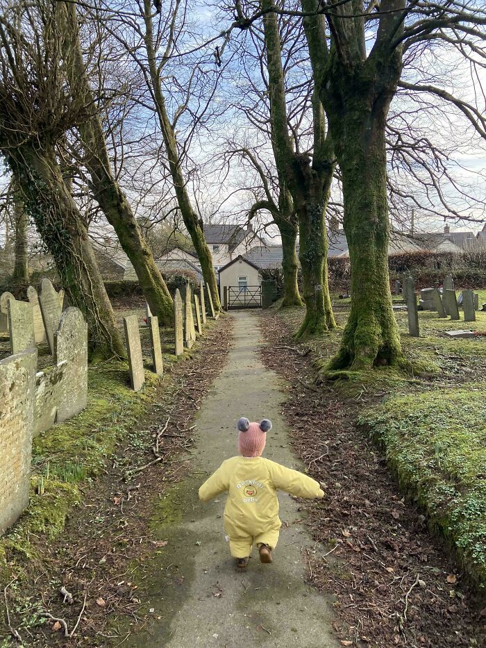 Toddler walking on a path between trees and gravestones, capturing a wholesome dad parenting moment outdoors.