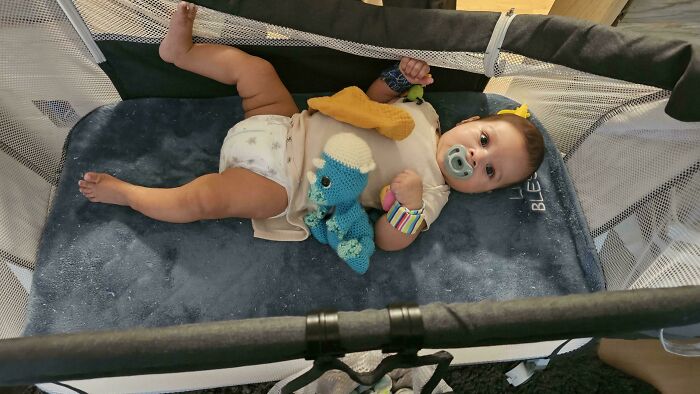 Baby lying in a portable crib with a pacifier and soft toys, capturing wholesome dads parenting moments.