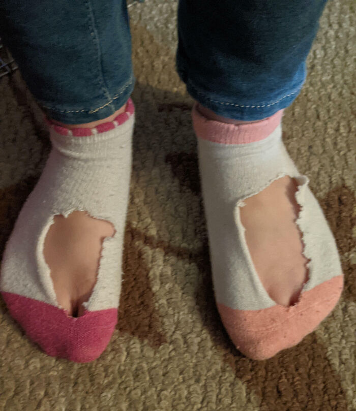 Worn-out socks with holes on child's feet, resembling clueless kids' fashion mishap.