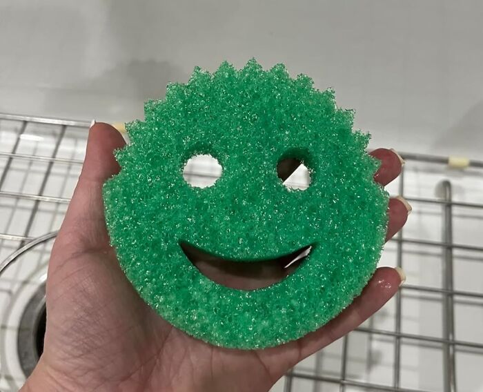 Hand holding a green smiley face sponge over a sink, inspired by Sharktank items.