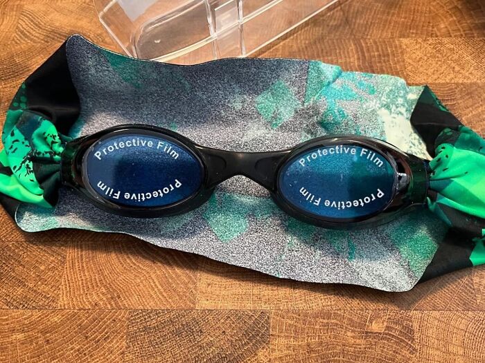 Swimming goggles with a protective film on a green and black patterned cloth, reminiscent of Sharktank items.