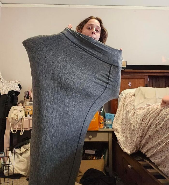 Person holding oversized gray leggings, reminiscent of a quirky Sharktank item, in a cluttered bedroom setting.