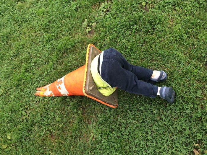 Niño atrapado de manera divertida en un cono de tráfico sobre el césped.