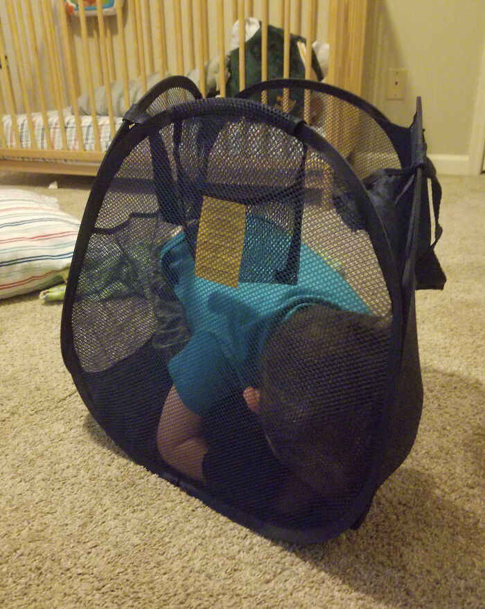 Niño atrapado en una cesta de lavandería, mostrando una de las tonterías divertidas que hacen los niños.