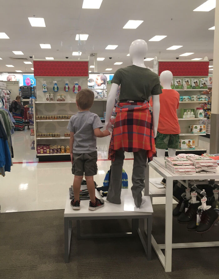 Niño sosteniendo la mano de un maniquí en una tienda, creando una escena divertida.