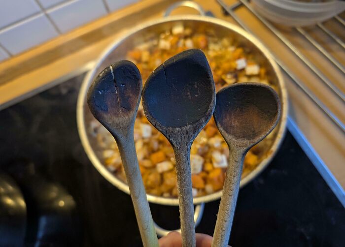 Three cool old wooden spoons in front of a pot, showcasing vintage kitchenware charm.