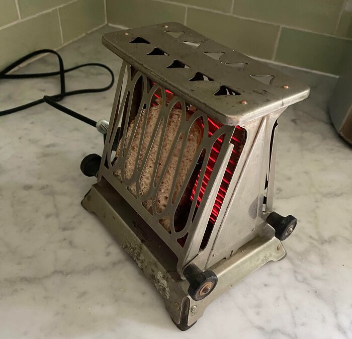 Vintage toaster on a marble counter, glowing red with a slice of bread. Cool-Old-Things.