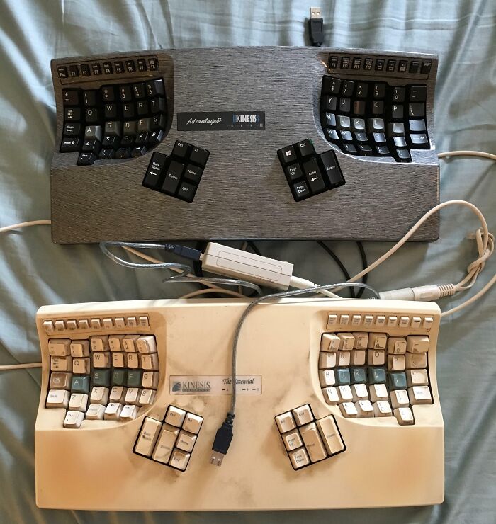Cool-old-things: Two vintage ergonomic keyboards on a bed, one black and one white, both with unique key layouts.