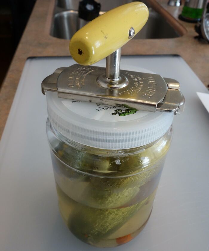 Old jar opener with a yellow handle on a pickle jar.