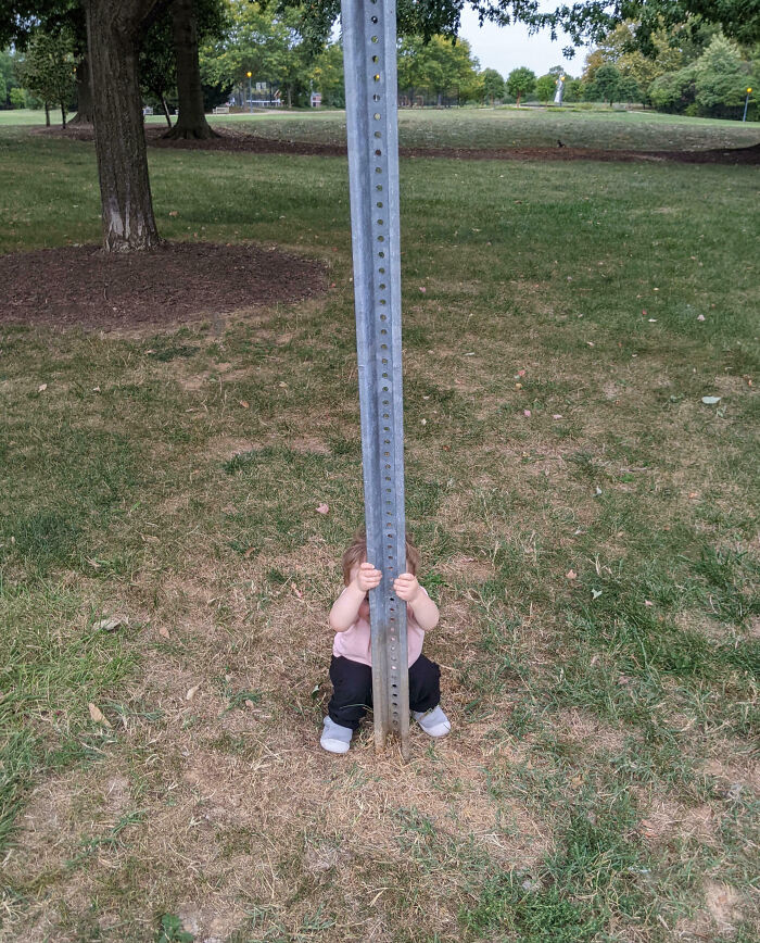 Niño escondido detrás de un poste en el parque, mostrando una divertida tontería infantil.