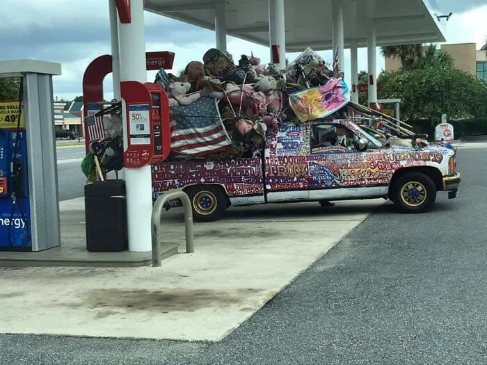 A uniquely decorated truck covered in flags and items at a Florida gas station, capturing a wild moment.
