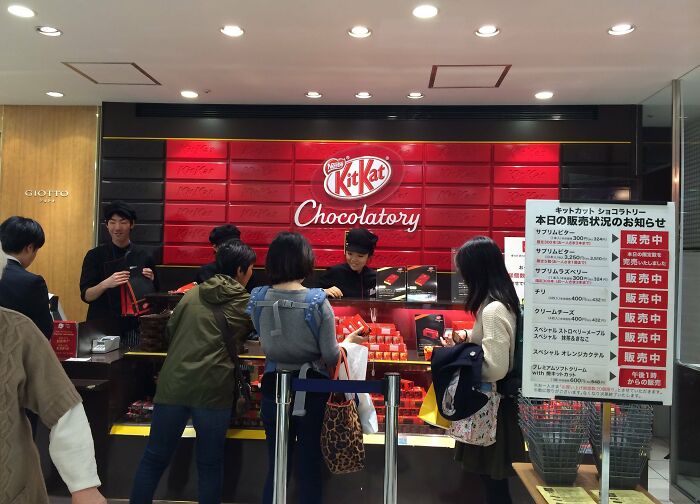 People shopping at a Kit Kat Chocolatory store in Japan, displaying a variety of unique Kit Kat flavors.