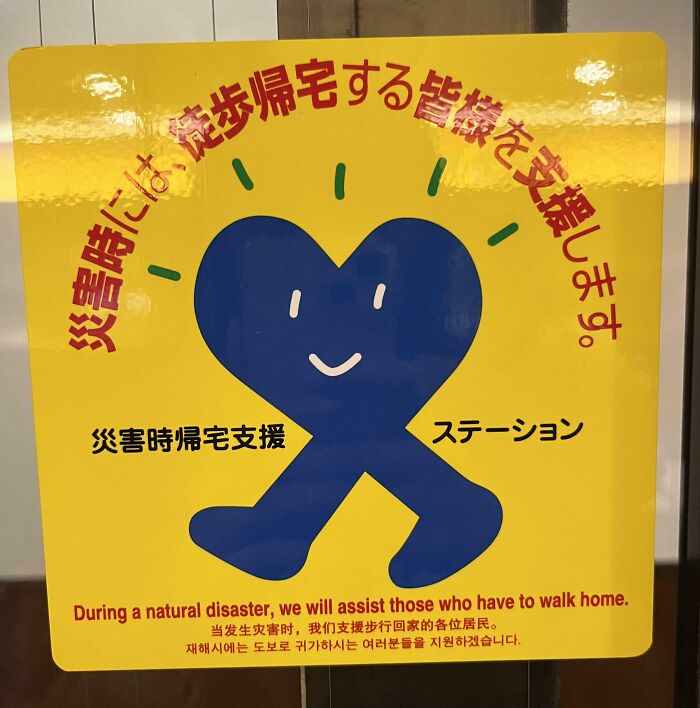 Yellow sign in Japan showing a blue heart with legs, offering assistance to pedestrians during disasters.