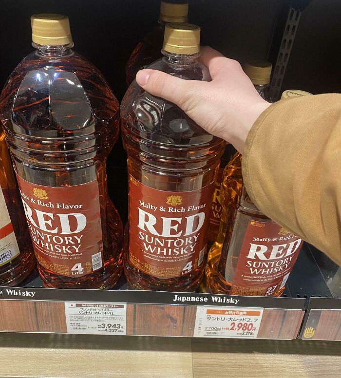 Hand grabbing a large bottle of Red Suntory Whisky on a store shelf, labeled Japanese Whisky, capturing interesting Japan pics.
