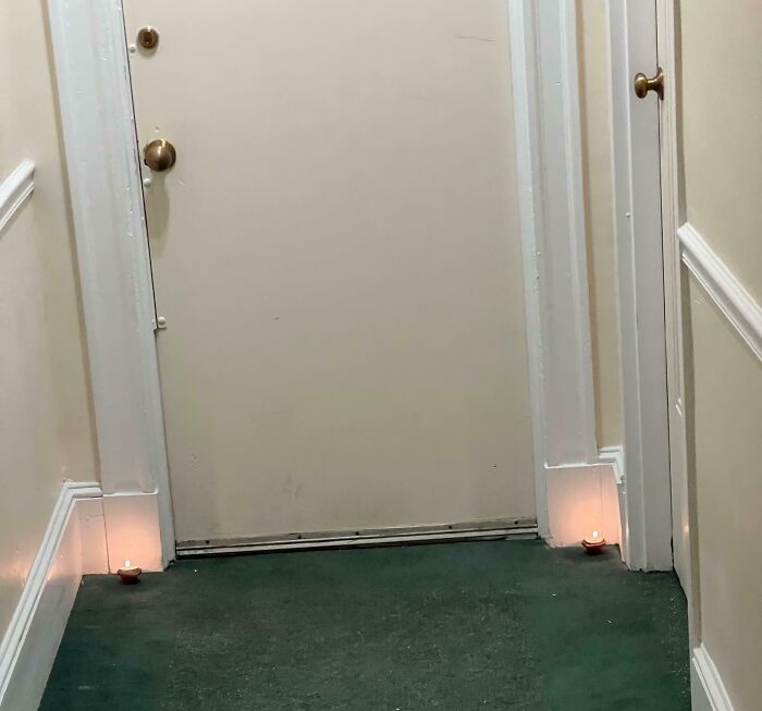 Two small candles placed outside a closed door in a hallway, highlighting a neighbor's horrific behavior.