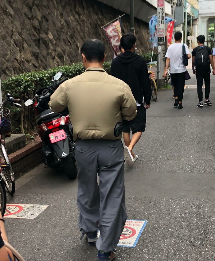 A man in a unique air-conditioned jacket walking on a street in Japan, showcasing interesting fashion.