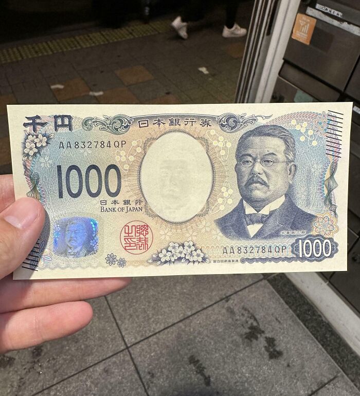 Person holding a 1000 yen Japanese banknote, showcasing interesting Japan pics in a city street setting.
