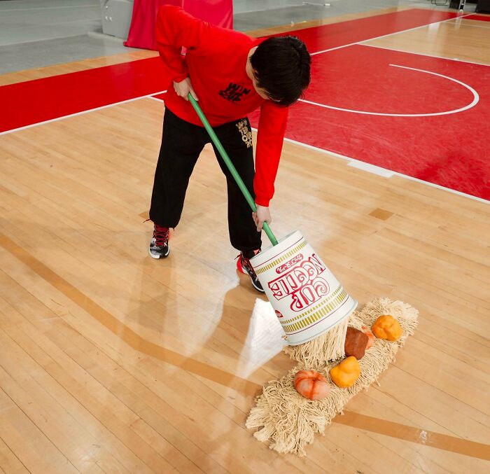 Person sweeping with a Cup Noodles-themed mop on a basketball court, showcasing interesting Japan pics.