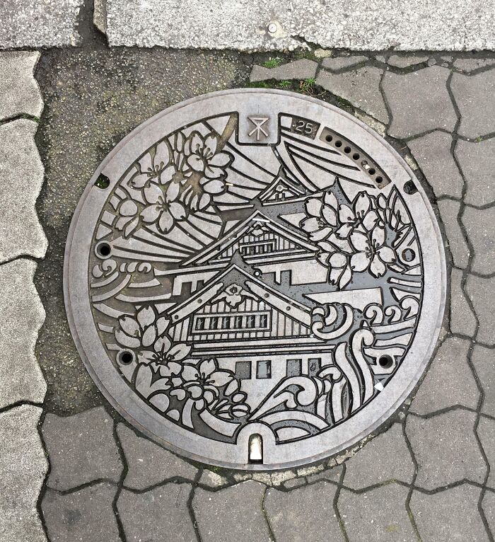 Decorative Japanese manhole cover with intricate designs, showcasing traditional architecture and cherry blossoms.