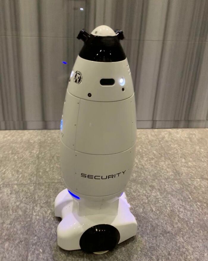 Security robot in Japan, sleek white design with a camera, patrolling an indoor area.