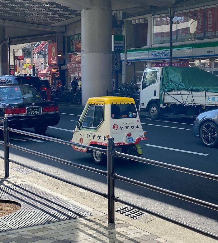 Small three-wheeled vehicle on a busy street in Japan, showcasing Interesting-Japan-Pics.