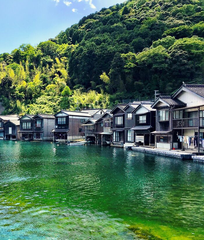 Traditional boathouses line the scenic waters of Ine Village in Japan, surrounded by lush green hills.