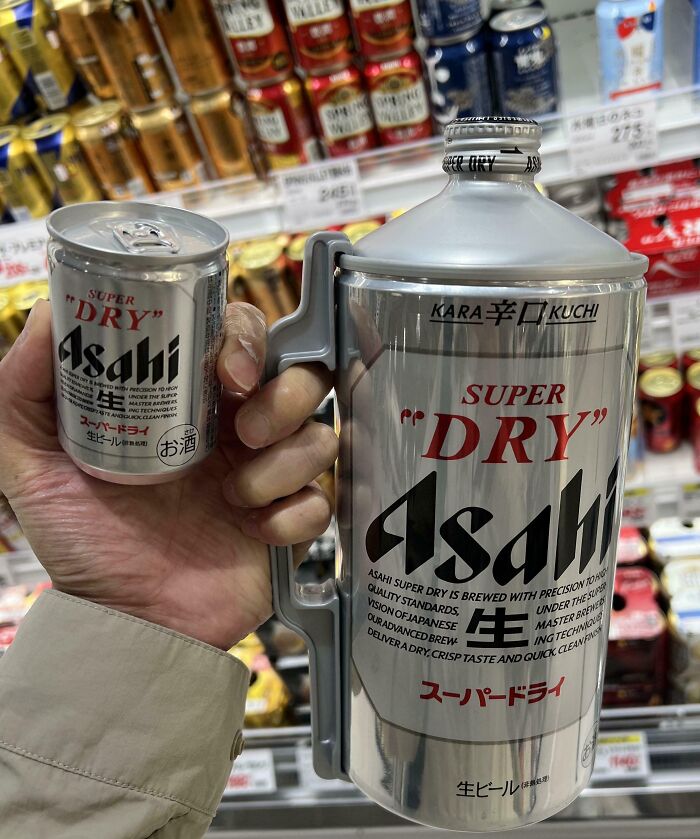 Man holding a tiny and a large Asahi Super Dry can in a Japanese store, showcasing Interesting Japan Pics.