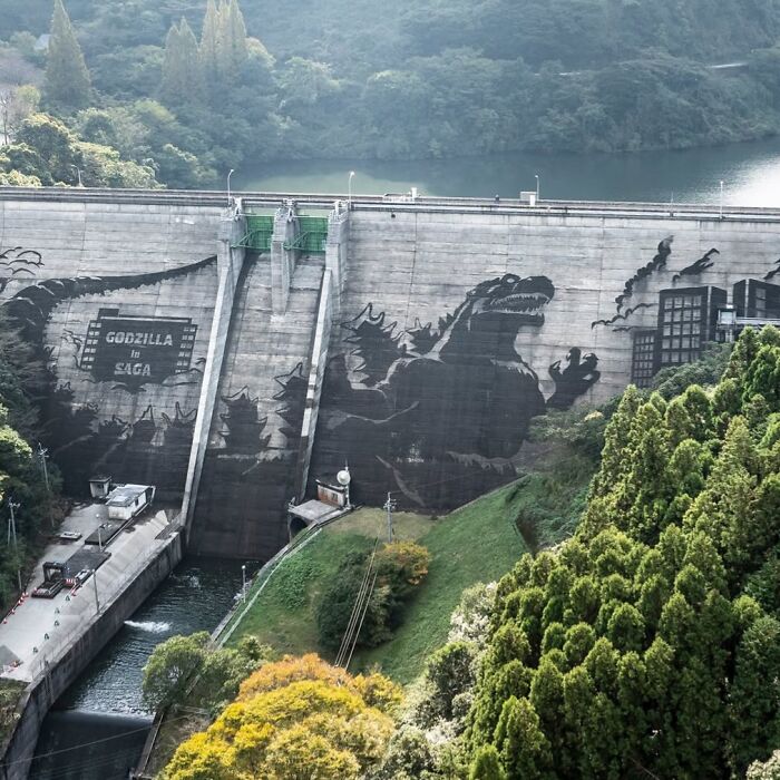 Godzilla mural on a dam in Japan, surrounded by lush greenery, showcasing interesting Japan pics.