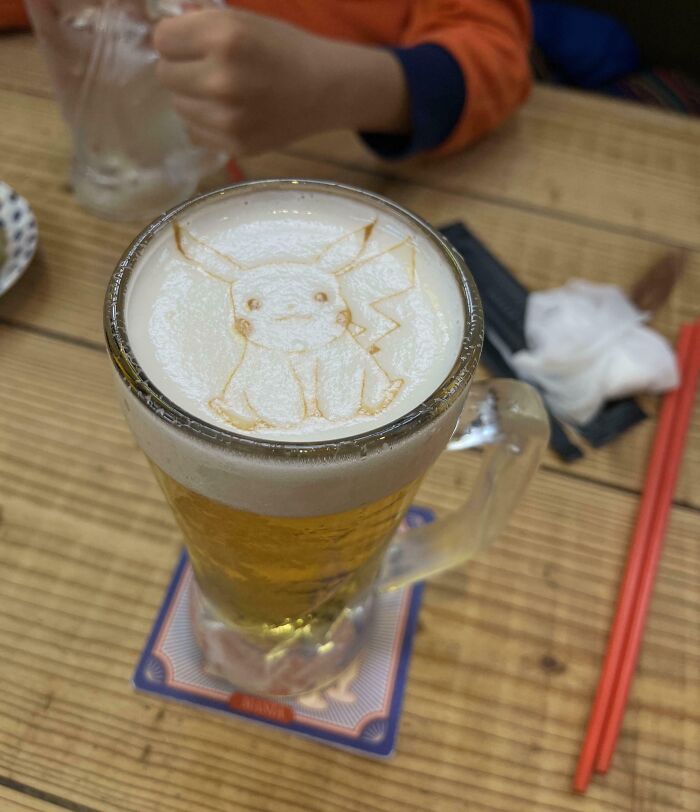 Interesting Japan Pics: Beer with Pikachu latte art on foam and red chopsticks on a wooden table.