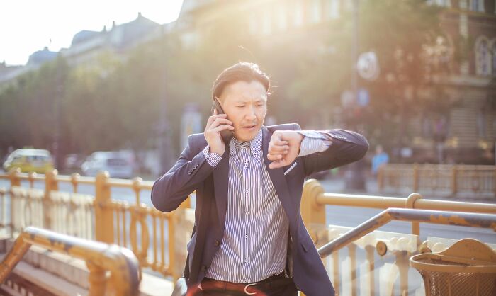 Man in a suit talking on the phone, glancing at his watch, representing busy office life humor.