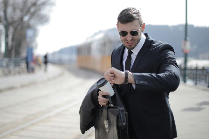 Man in suit checks watch, holding coffee and briefcase, embodying jokes-about-office rush.