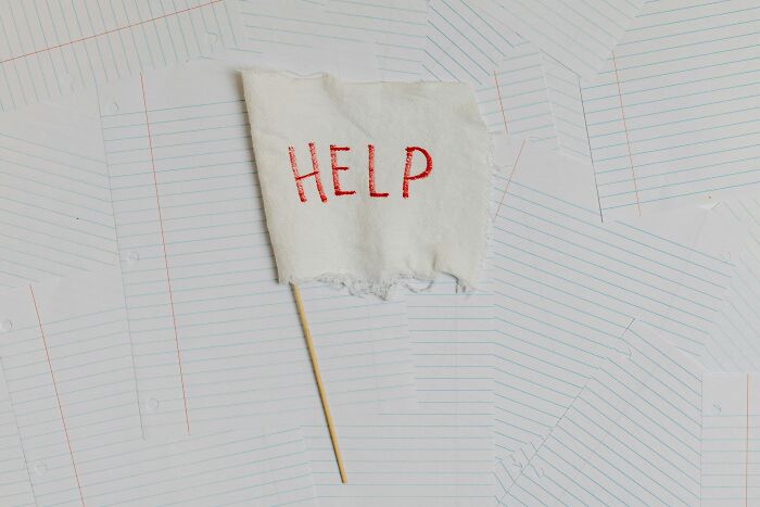 A white flag with "HELP" written on it sticks out from a stack of lined paper, humorously depicting office distress.