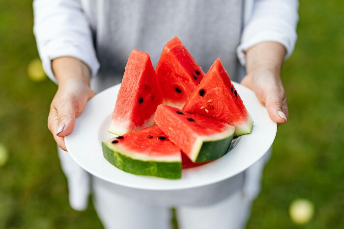 A person holding a plate of sliced watermelon, a health-boosting fruit, outdoors.