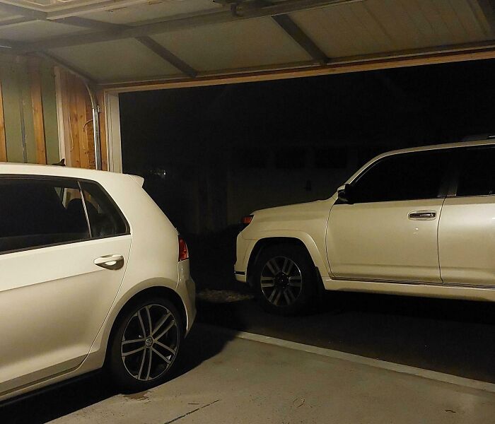 Two white SUVs parked closely in a garage, illustrating a frustrating neighbor parking issue for shaming neighbors.