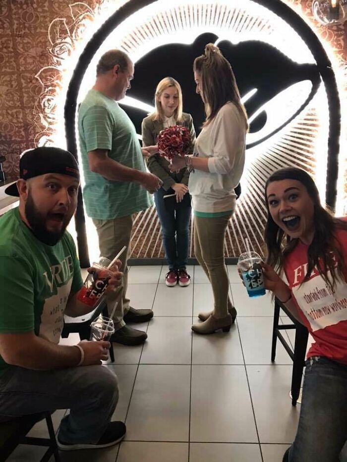 Casual ceremony in front of a large Taco Bell logo, with guests holding slushies; a humorous budget-wedding-fails moment.