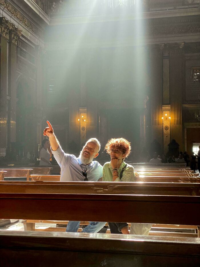 Two people sitting in a sunlit church, with one pointing upwards, resembling an accidental renaissance painting.