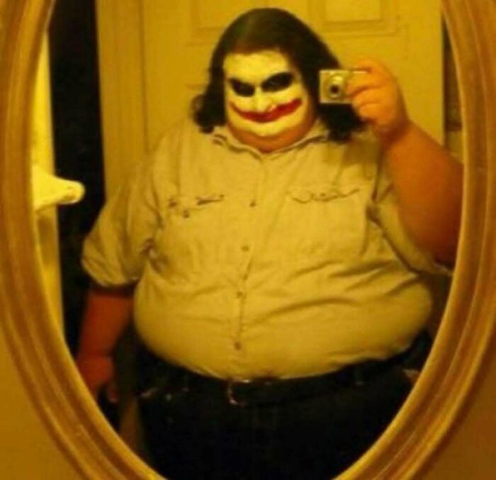 Person with Joker face paint taking a mirror selfie wearing a beige shirt, showcasing a weird side of the internet photo.