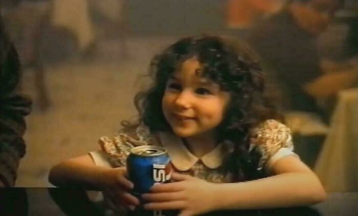 A smiling child in a floral dress enjoys a soda, capturing a joyful '90s moment.