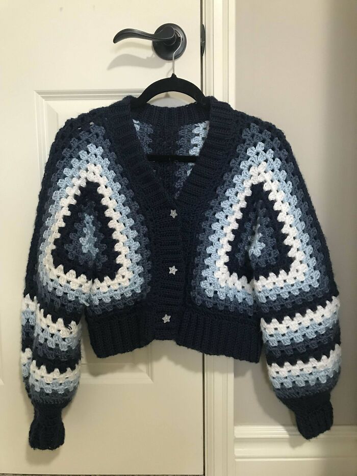 Crochet masterpiece cardigan in navy, light blue, and white granny square pattern hanging on a door hook.