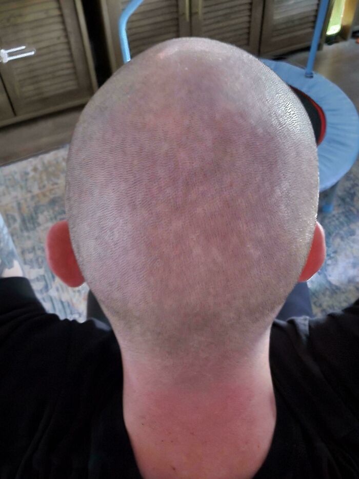 Bald dad seen from behind showing a close-up of his head in a casual home setting, capturing a parenting moment.