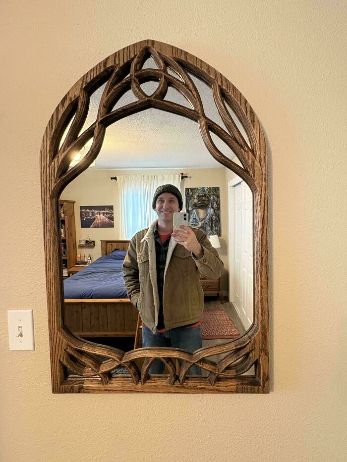 Man taking a mirror selfie framed by intricate woodworking project, showcasing impressive craftsmanship.