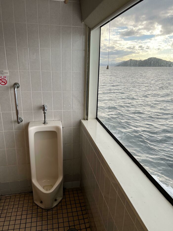 Urinal in a Japanese bathroom with large window overlooking the ocean, showcasing interesting views in Japan.