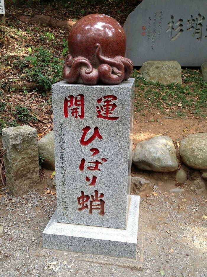Stone sculpture with an octopus design, featuring red inscriptions in a Japanese garden setting.