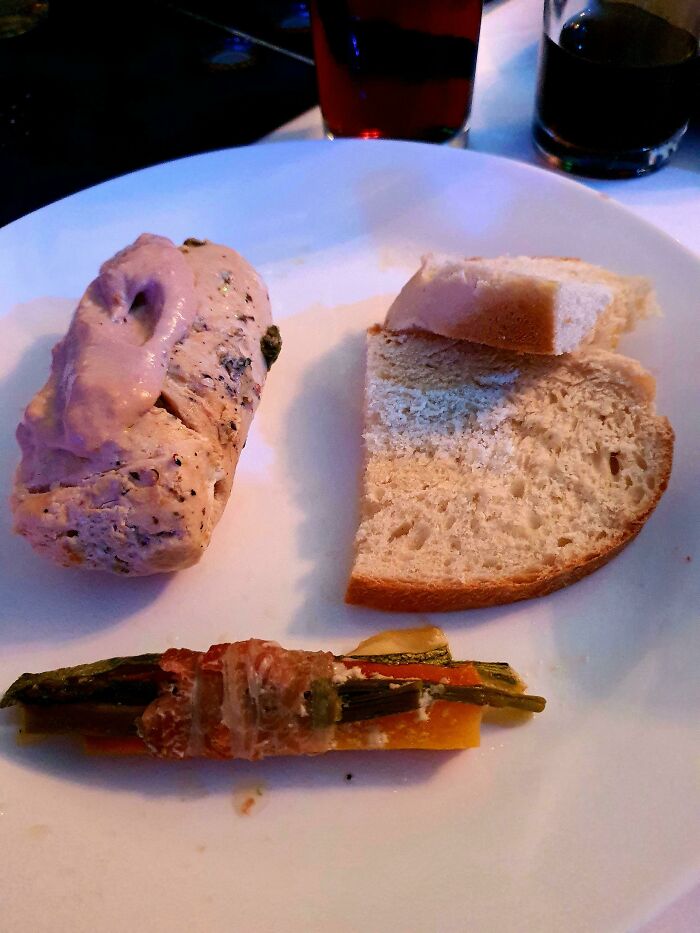 Plate of plain chicken, bread slice, and vegetable roll-up - a budget wedding meal example.