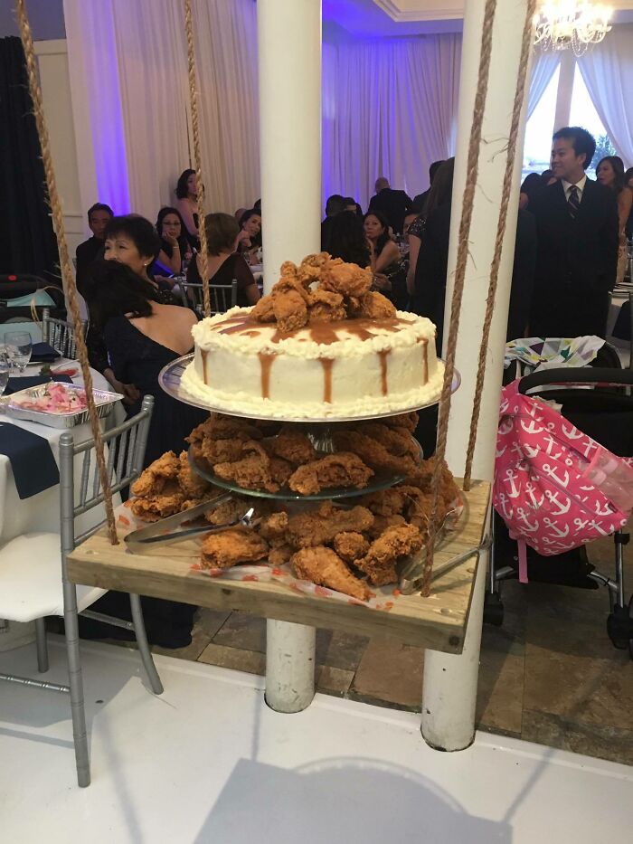 Wedding cake topped with fried chicken on a serving tray, surrounded by guests.