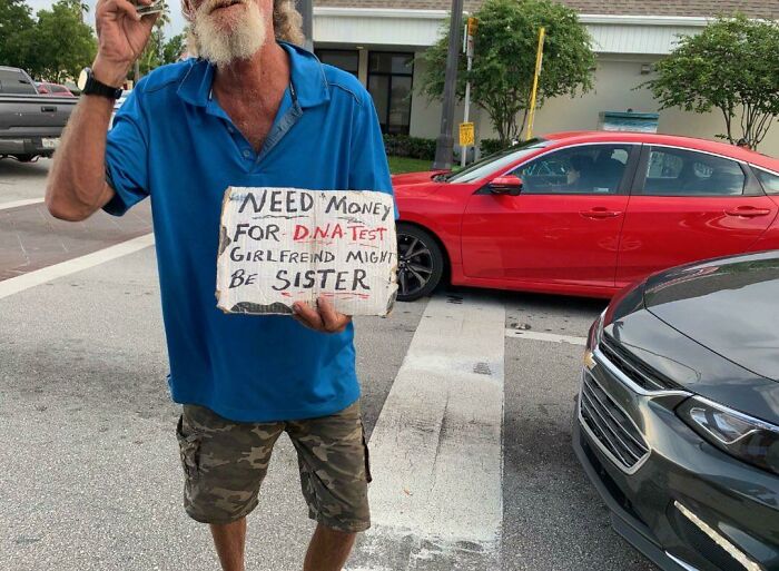 Man in camouflage shorts holding a humorous sign seeking money at Florida intersection, capturing wild moments.